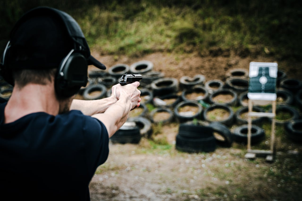 Adult male practicing target shooting outdoors with pistol at a range.