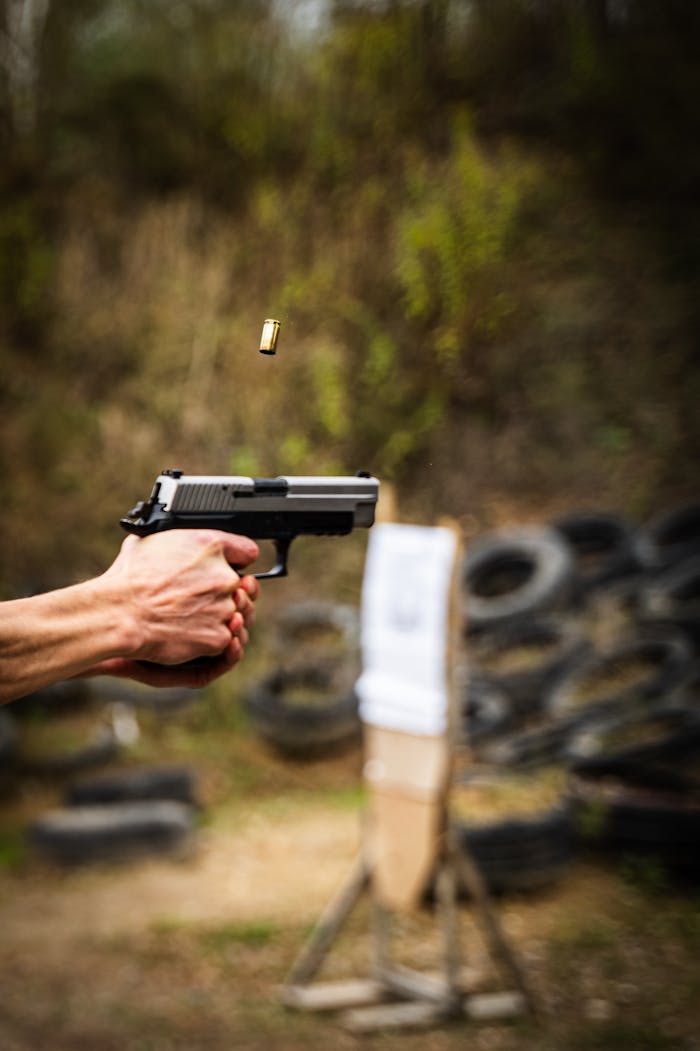 Close-up of a handgun firing at an outdoor shooting range, capturing the ejected cartridge in motion.