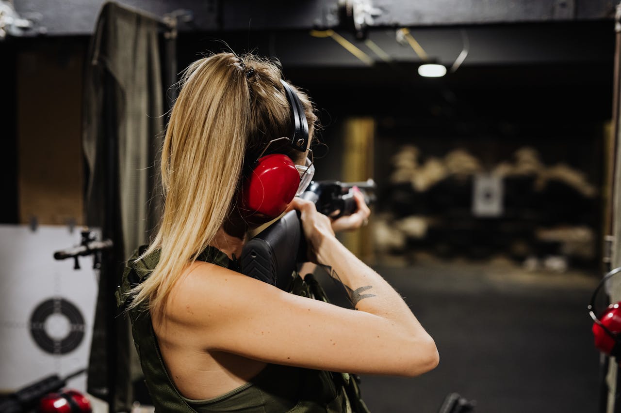 A woman aiming a rifle at a target in an indoor shooting range.