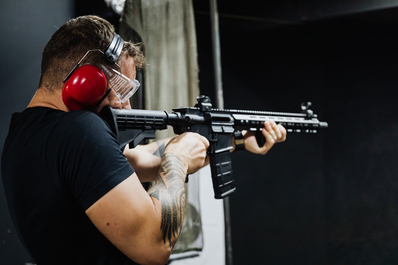 Man with earmuffs aiming a rifle at an indoor shooting range.